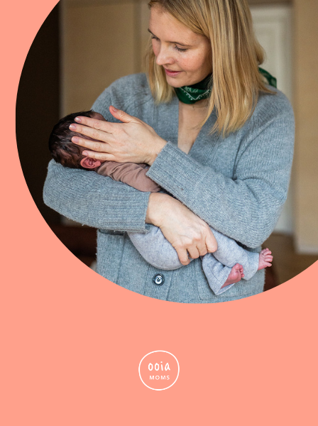 Mutter trägt ihr Baby im Arm und streicht mit der Hand über dessen Wange.