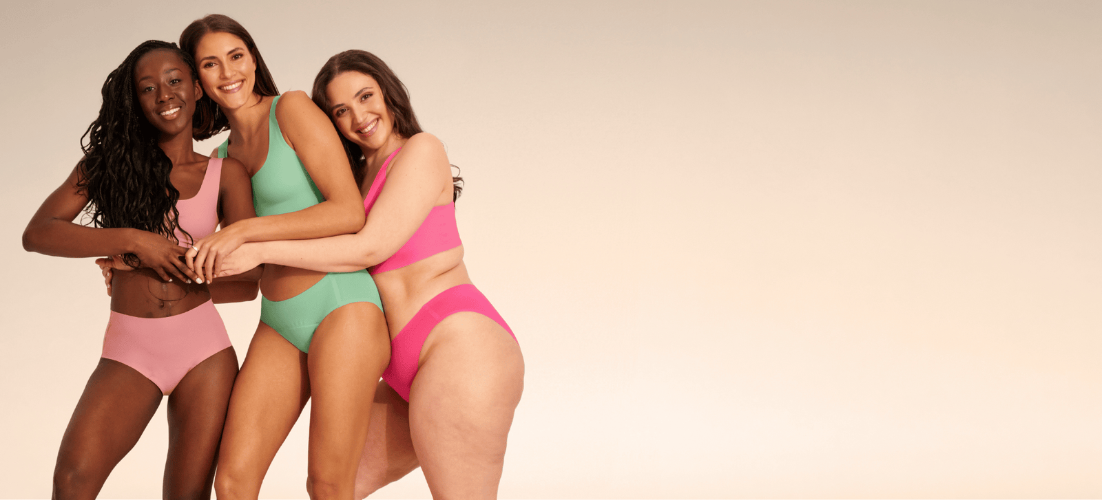Drei Models umarmen sich und tragen nahtlose Menstruationsunterwäsche in sage, rosa und pink