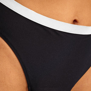 Modell trägt ooia Perioden Beachwear Slip in schwarz mit weißen Kontrastdetails.
detail