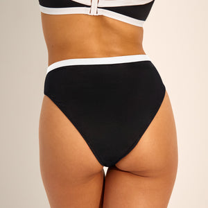 Modell trägt ooia Perioden Beachwear Slip in schwarz mit weißen Kontrastdetails.
Rückansicht