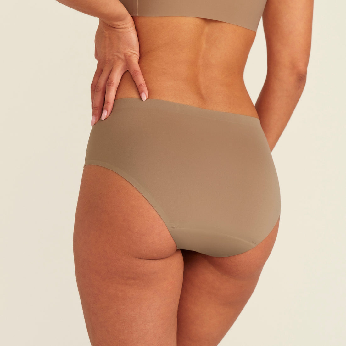 Modell trägt ooia Periodenunterwäsche Hipster Seamless in Taupe mit nahtlosem Design, Rückansicht