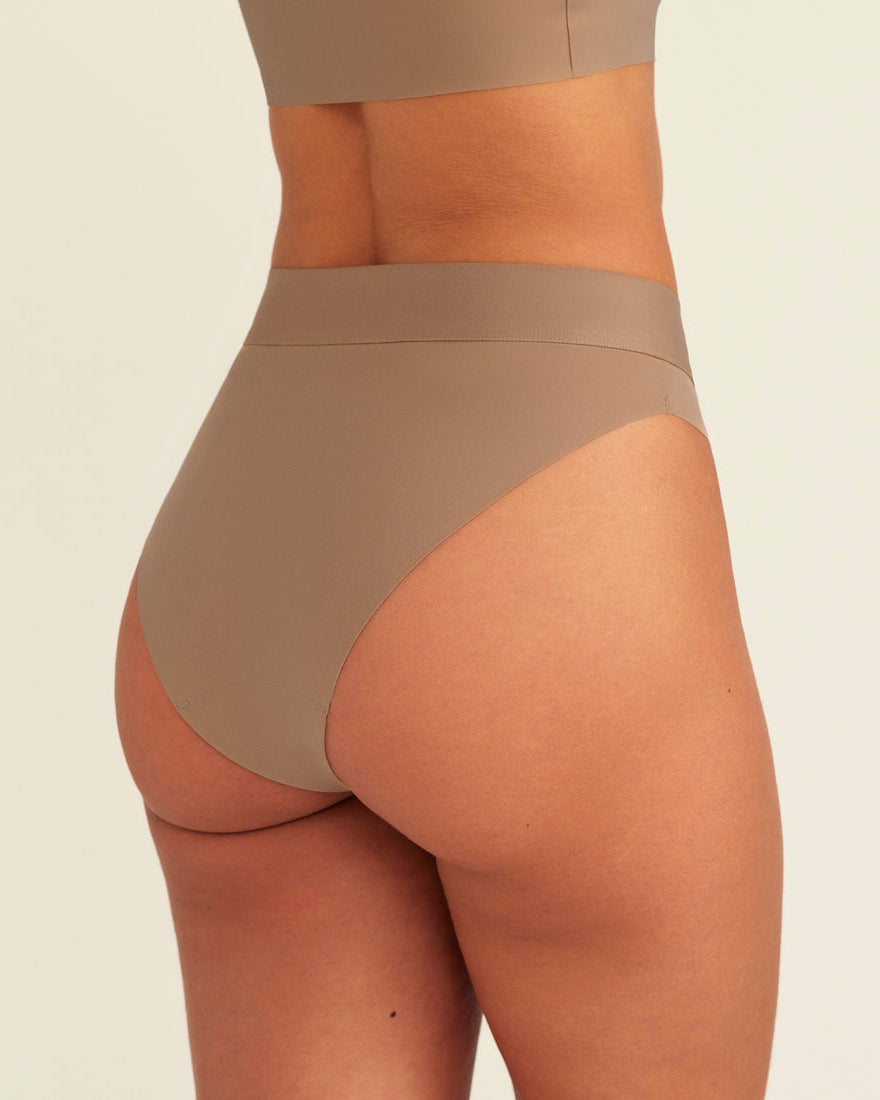 Modell trägt ooia Periodenslip Seamless Cheeky in Taupe mit hohem Beinausschnitt, Rückansicht