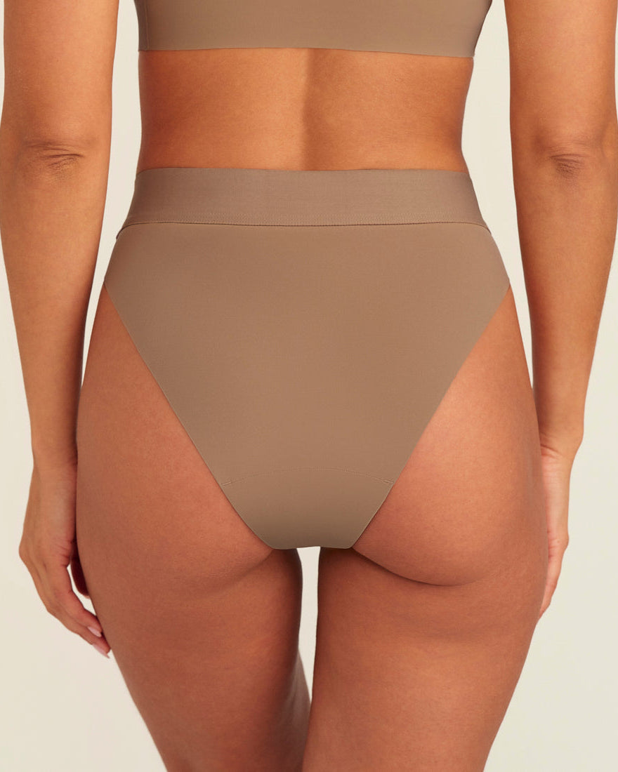 Modell trägt ooia Periodenslip Seamless Cheeky in Taupe mit hohem Beinausschnitt, Rückansicht