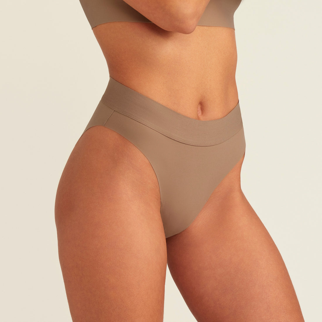 Modell trägt ooia Periodenslip Seamless Cheeky in Taupe mit hohem Beinausschnitt