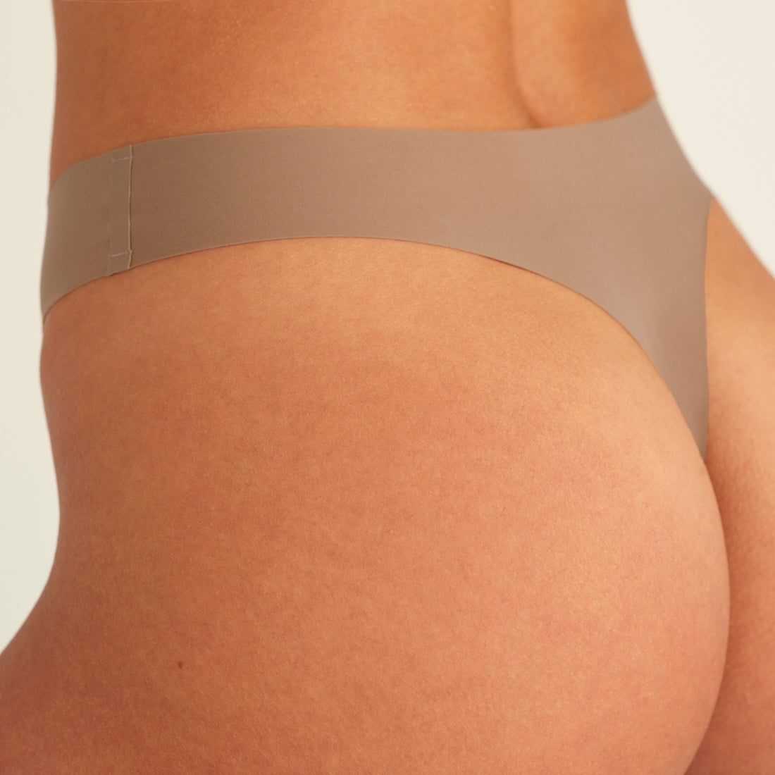 Modell trägt ooia Periodenunterwäsche String Seamless in Taupe mit leichter Saugstärke, Detailansicht nahtloses Design