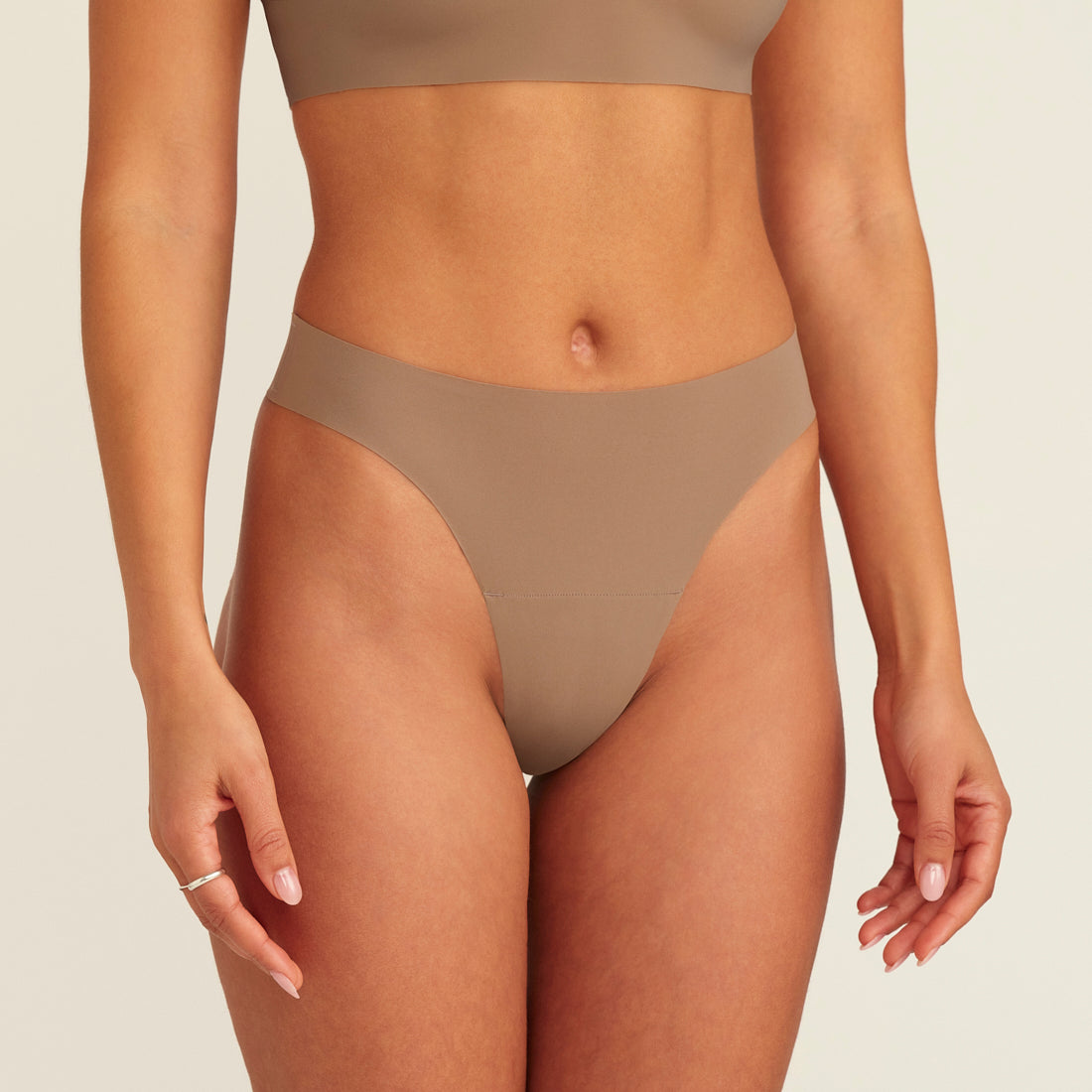 Modell trägt ooia Periodenunterwäsche String Seamless in Taupe mit leichter Saugstärke