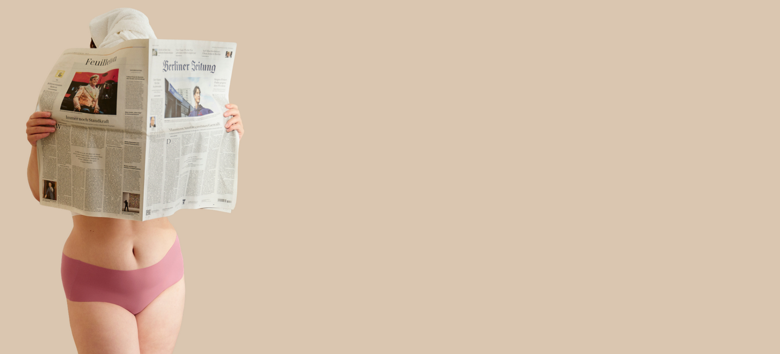 Model in rosaner nahtloser Periodenunterwäsche trägt Handtuch-Turban und hält eine Zeitung