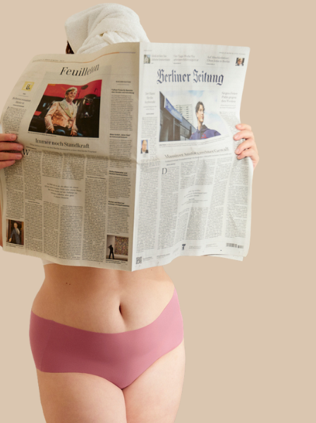 Model in rosaner nahtloser Periodenunterwäsche trägt Handtuch-Turban und hält eine Zeitung