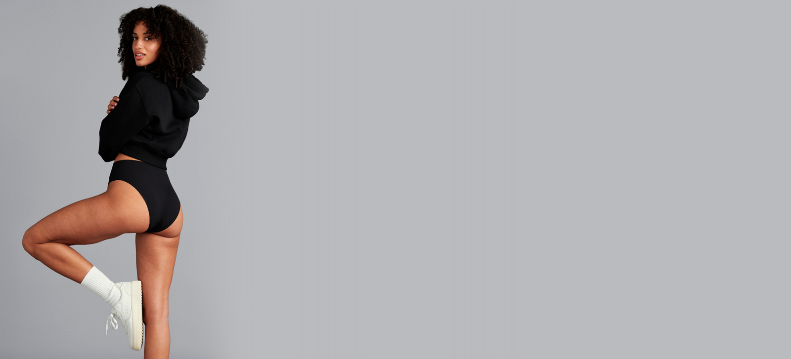 Model macht eine Yogapose in schwarzer nahtloser Periodenunterwäsche und einem schwarzen Hoodie.