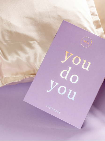 Person schreibt in das lilane you do you Booklet von ooia