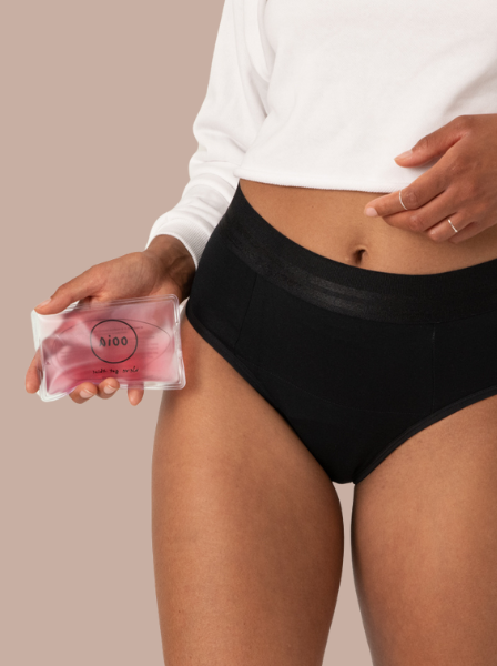 Model trägt schwarze Periodenunterwäsche und hält Heatpad in der Hand
