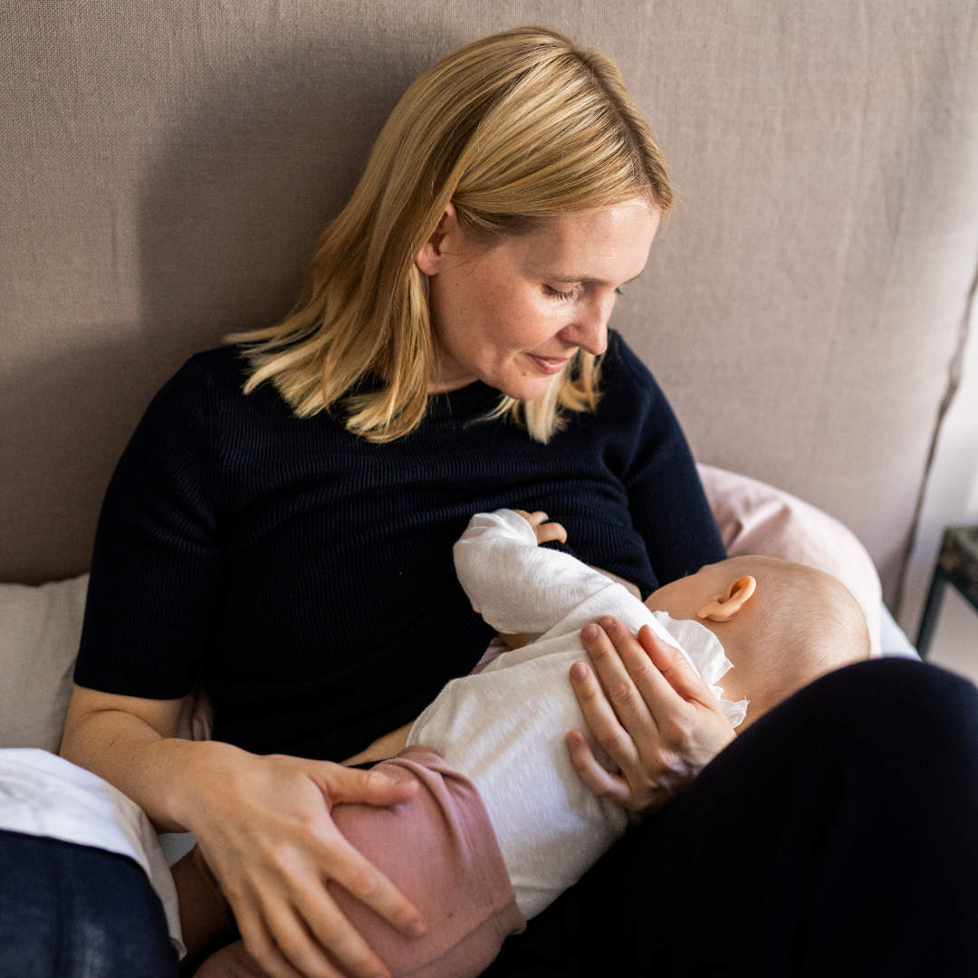 Mutter sitzt im Bett und stillt ihr Baby.