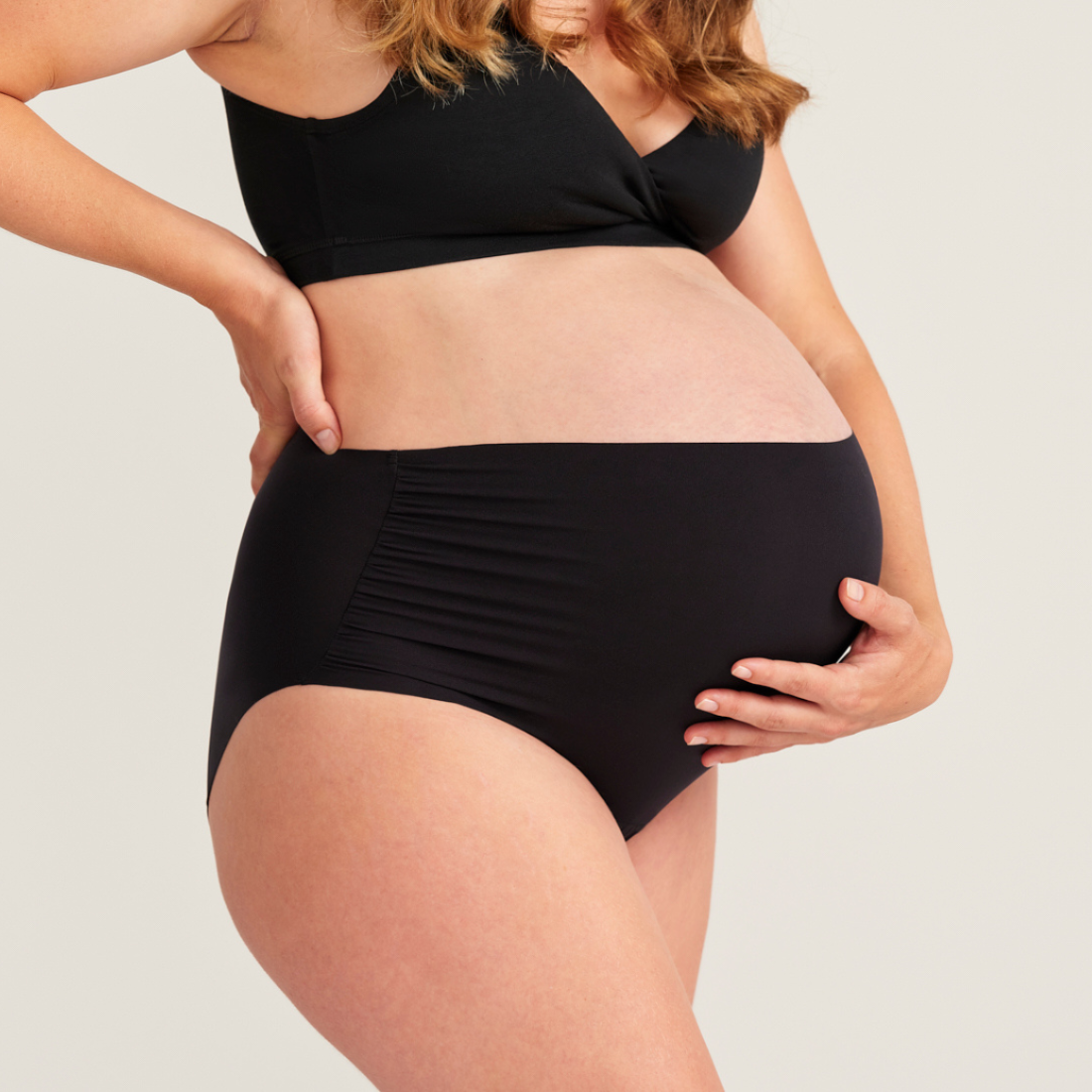 Modell trägt schwarzen ooia Moms BH und ooia The Belly Hugger Schwangerschafts-Panty in Schwarz mit hohem Bund
