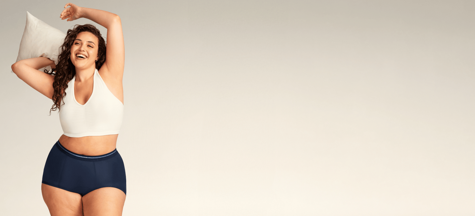 Model trägt eine dunkelblaue Perioden-Shorty von ooia und hält dabei lachend ein Kissen in der Hand