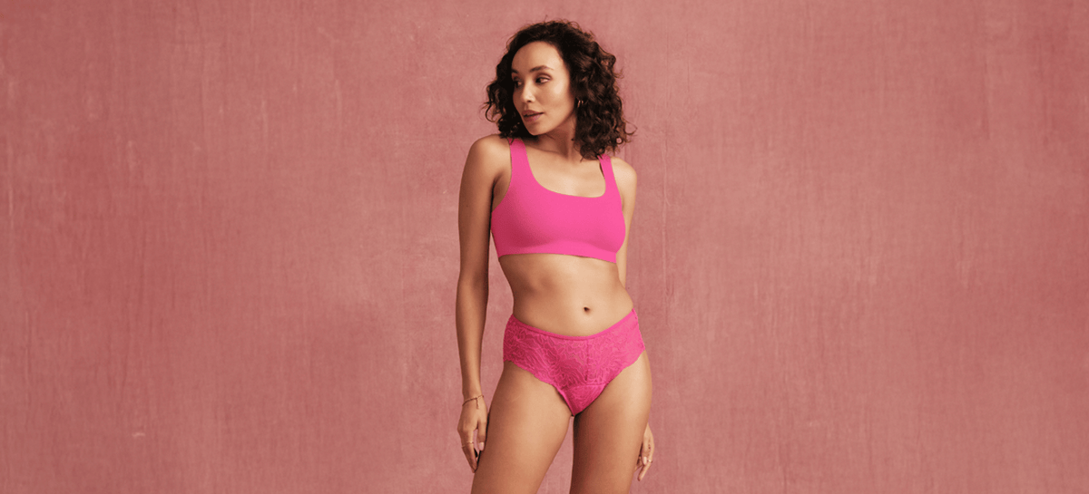 Model steht vor rosa Hintergrund und trägt einen Lace Menstruationsslip in hot pink von ooia.