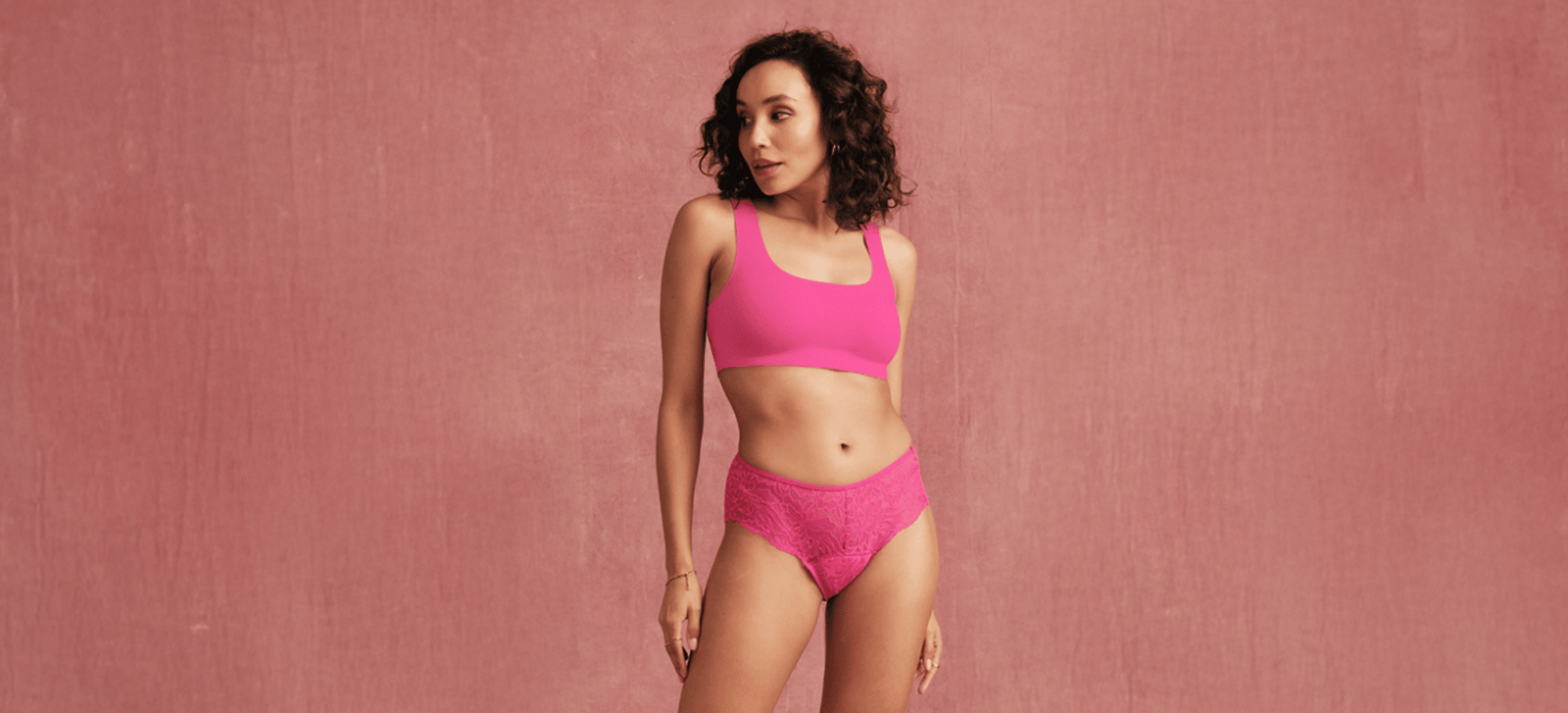 Model steht vor rosa Hintergrund und trägt einen Lace Menstruationsslip in hot pink von ooia.
