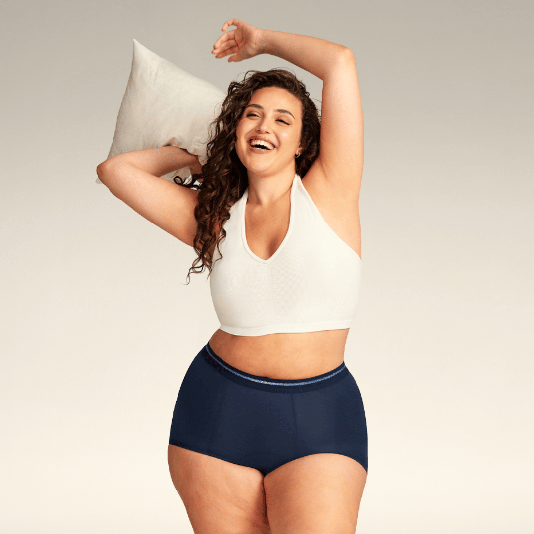 Model trägt eine dunkelblaue Perioden-Shorty von ooia und hält dabei lachend ein Kissen in der Hand