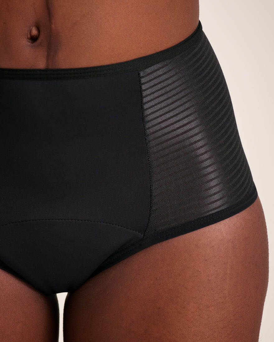 Modell trägt ooia Highwaist Extra Strong in Schwarz – Periodenunterwäsche mit hohem Bund und Glanzdetail. Detailansicht.
