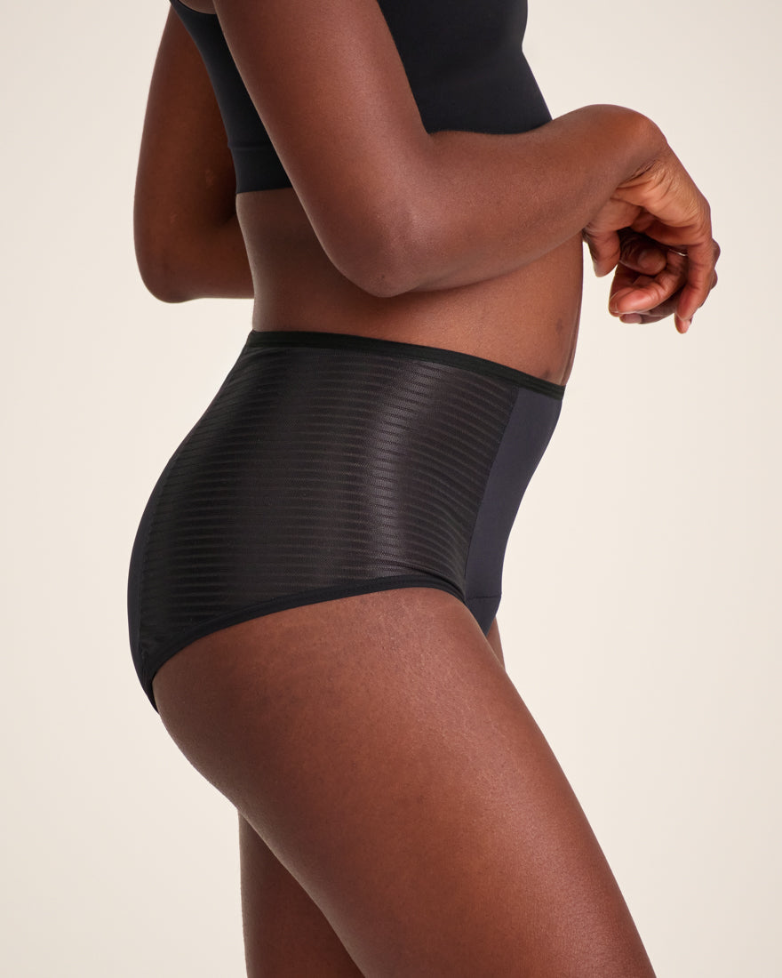 Modell trägt ooia Highwaist Extra Strong in Schwarz – Periodenunterwäsche mit hohem Bund und Glanzdetail.