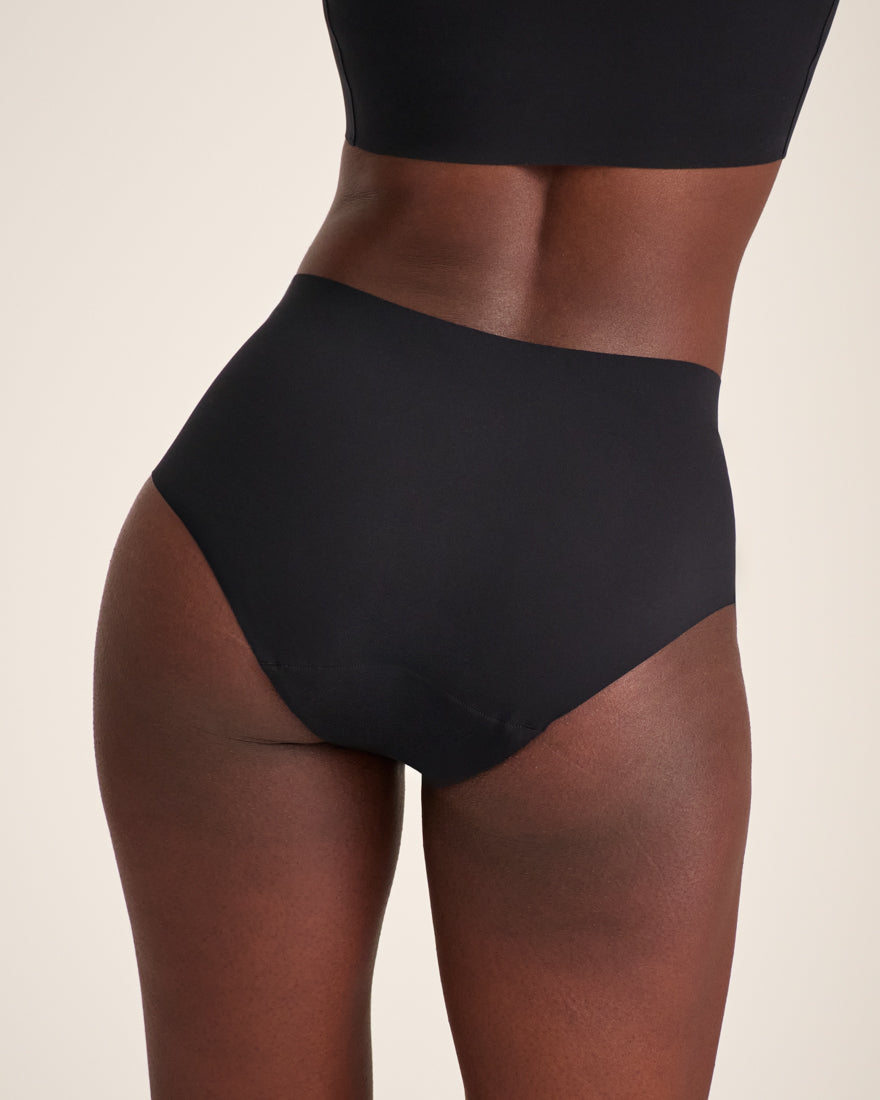 Modell trägt ooia Highwaist Seamless in Schwarz – nahtlose Periodenunterwäsche mit hohem Bund. Rückansicht.