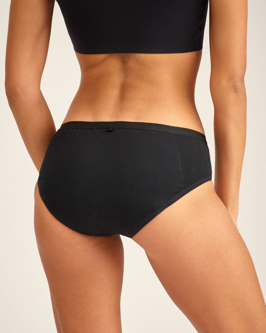 Modell trägt ooia Hipster in Schwarz – Periodenunterwäsche. Rückansicht.