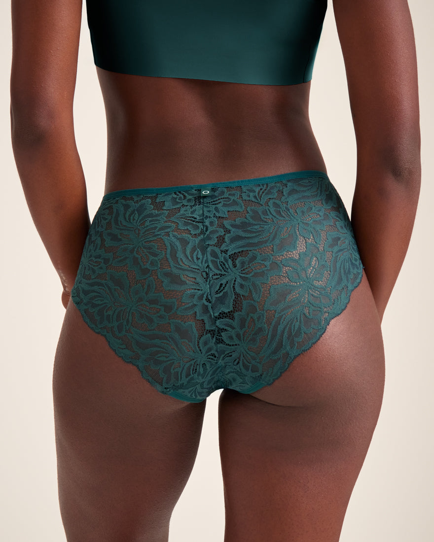 Modell trägt ooia Hipster Allover Lace in Grün – elegante Periodenunterwäsche mit durchgehender Spitze. Rückansicht.