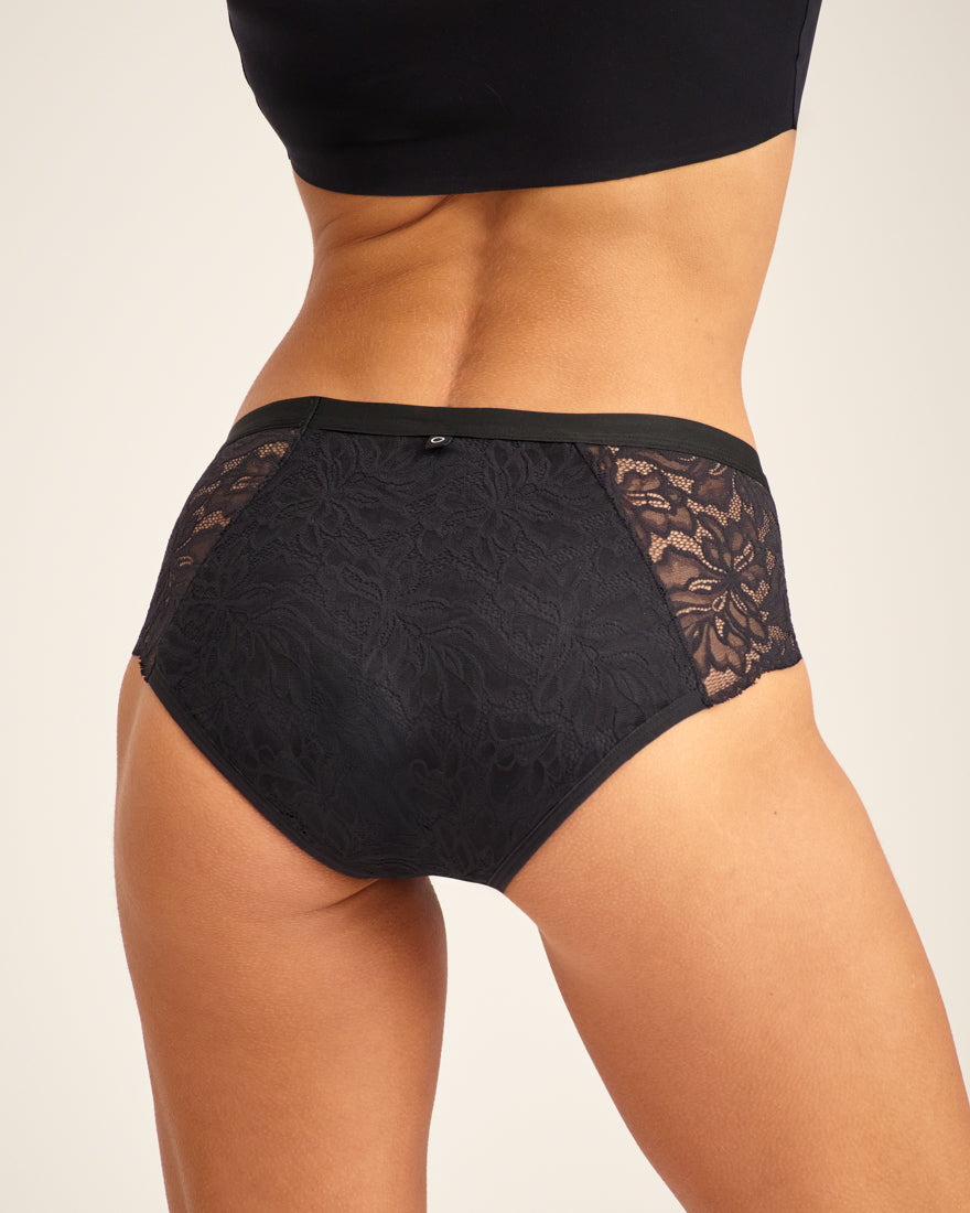 Modell trägt ooia Hipster Allover Lace Extra Strong in Schwarz - Periodenunterwäsche mit durchgehender Spitze und starker Saugstärke. Rückansicht.