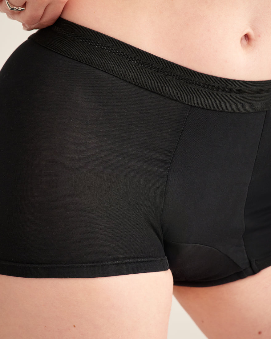 Modell trägt ooia Shorty Extra Strong in Schwarz – Periodenunterwäsche mit breitem Bund und starker Saugstärke.