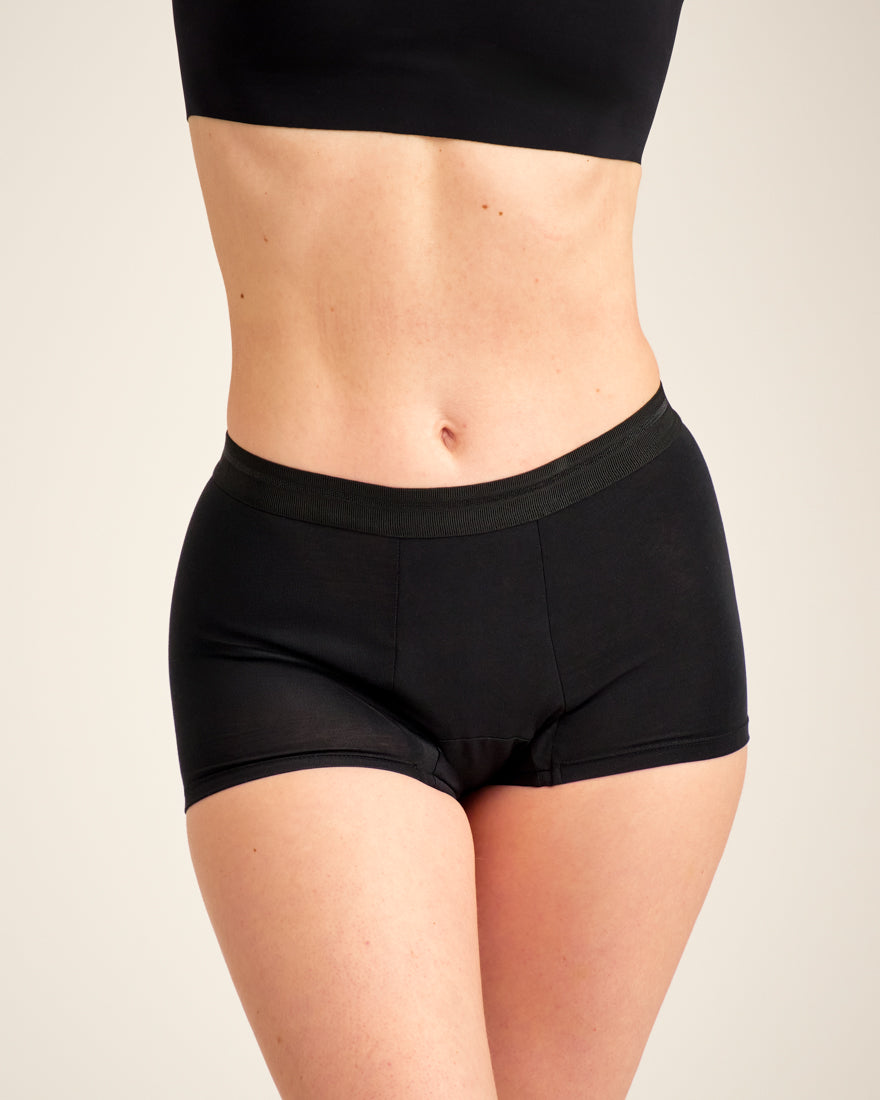 Modell trägt ooia Shorty Extra Strong in Schwarz – Periodenunterwäsche mit breitem Bund und starker Saugstärke.