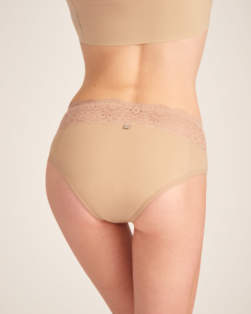 Modell trägt ooia Slip in Beige - Periodenunterwäsche mit breitem Spitzenbund im klassischen Schnitt. Rückansicht.