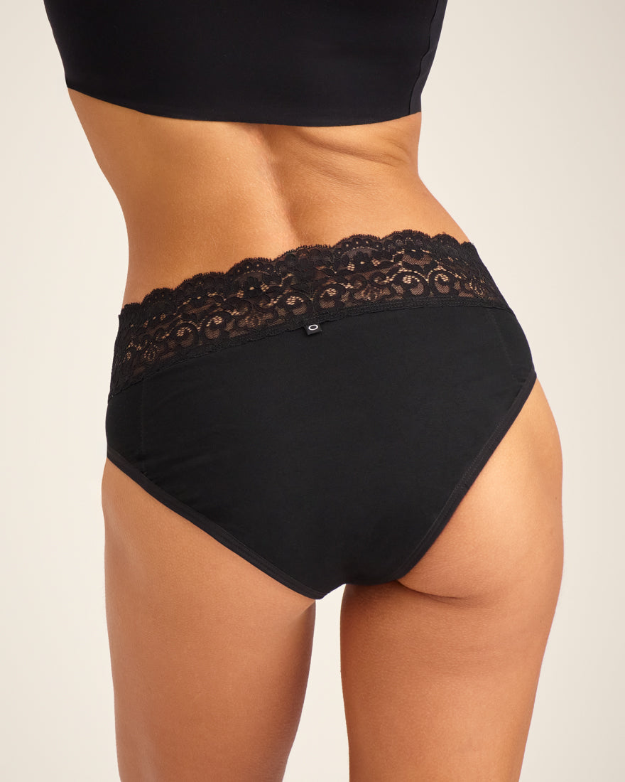 Modell trägt ooia Slip Extra Strong in Schwarz – Periodenunterwäsche mit breitem Spitzenbund im klassischen Schnitt. Rückansicht.
