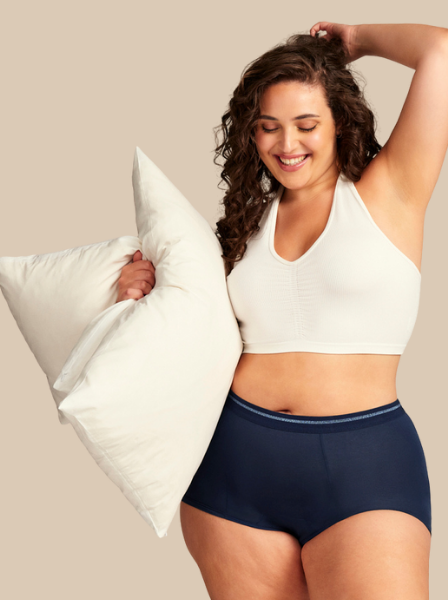 Model in Periodenunterwäsche Shorty in dunkelblau hält Kissen unter dem Arm