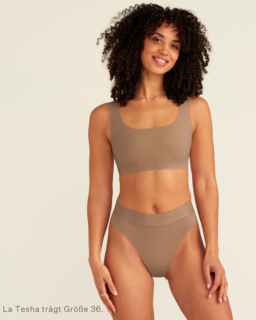 Modell trägt ooia Periodenslip Seamless Cheeky in Taupe mit hohem Beinausschnitt