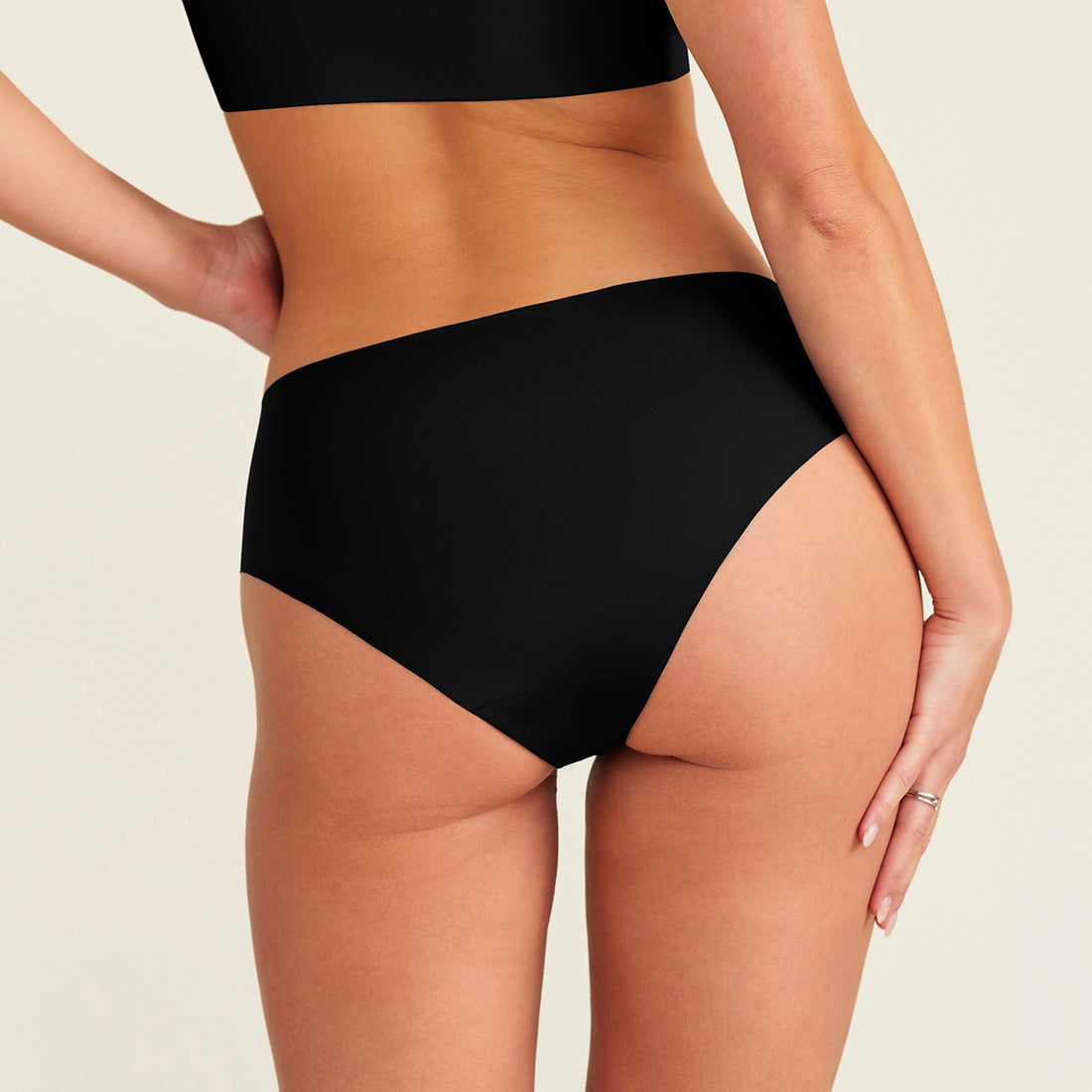 Modell trägt ooia everyday Hipster Seamless in Schwarz - nahtlose Unterwäsche die Slipeinlagen ersetzt. Rückansicht.