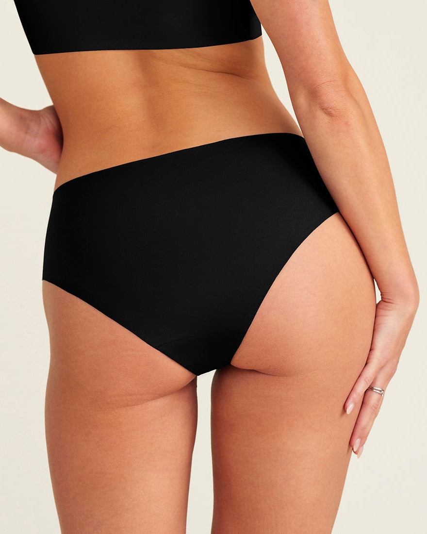 Modell trägt ooia everyday Hipster Seamless in Schwarz – nahtlose Unterwäsche, die Slipeinlagen ersetzt. Rückansicht.