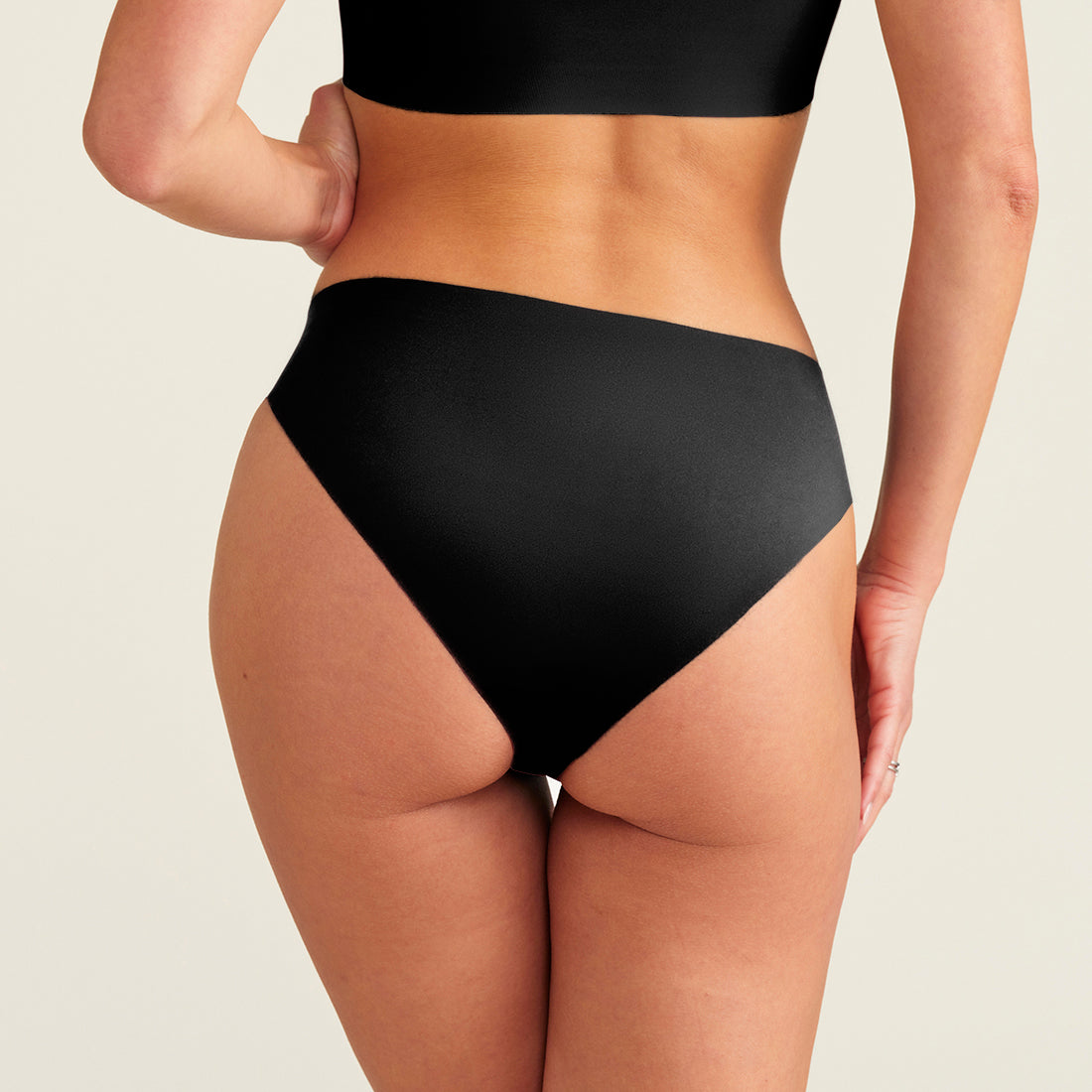 Modell trägt ooia everyday Slip Seamless in Schwarz – nahtlose Unterwäsche, die Slipeinlagen ersetzt. Rückansicht.