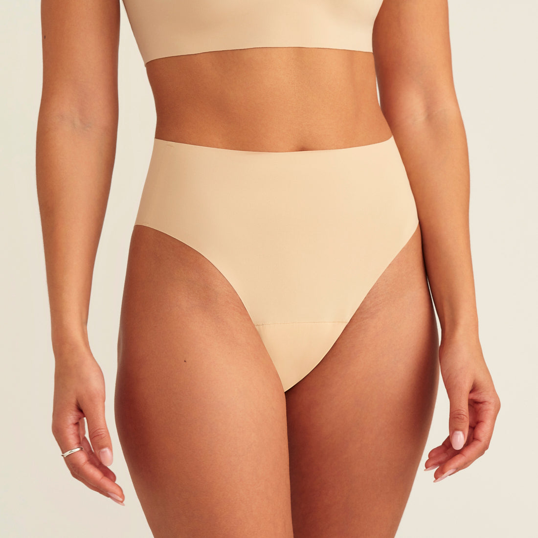 Modell trägt ooia Perioden Highwaist Seamless Cheeky in Beige – nahtloser Slip mit hoher Taille und Beinausschnitt