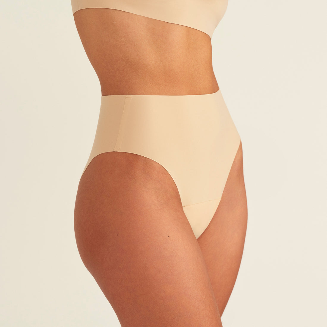 Modell trägt ooia Perioden Highwaist Seamless Cheeky in Beige – nahtloser Slip mit hoher Taille und Beinausschnitt