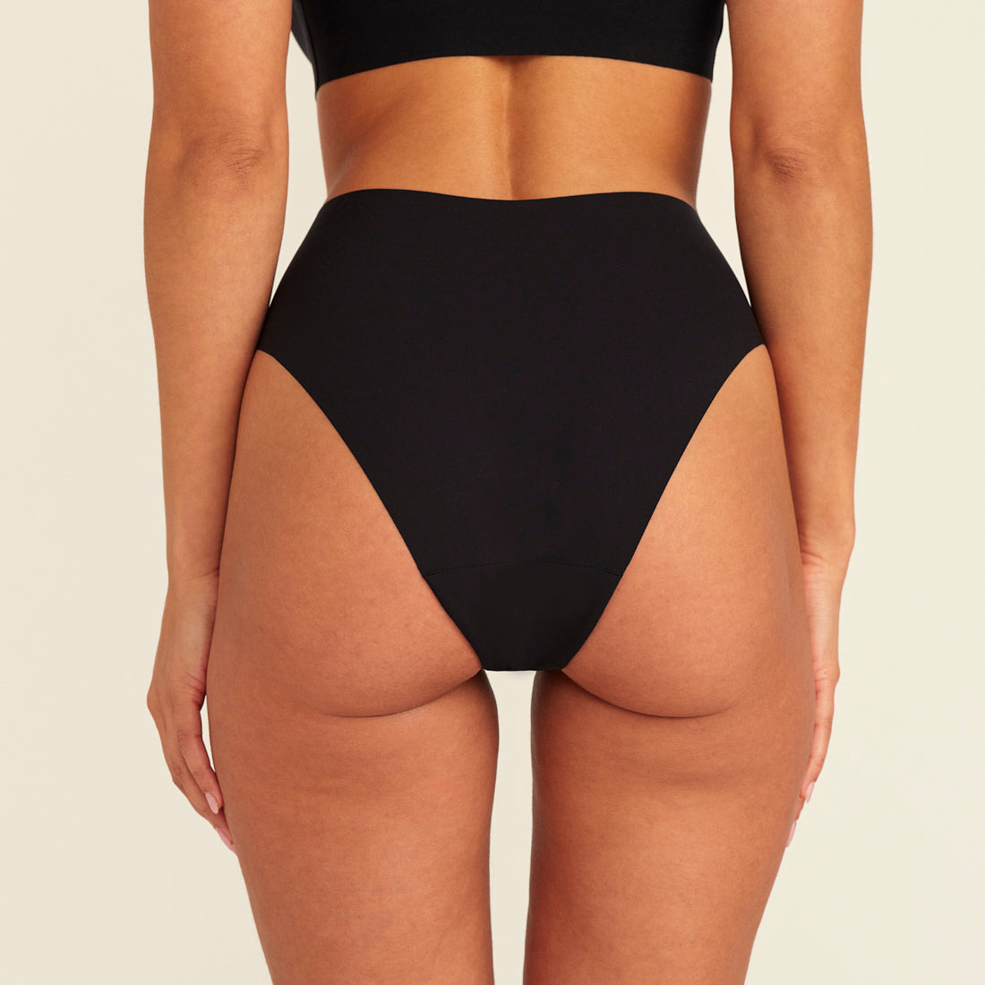 Modell trägt ooia Highwaist Seamless Cheeky in Schwarz – nahtloser Slip mit hoher Taille und Beinausschnitt, Rückansicht
