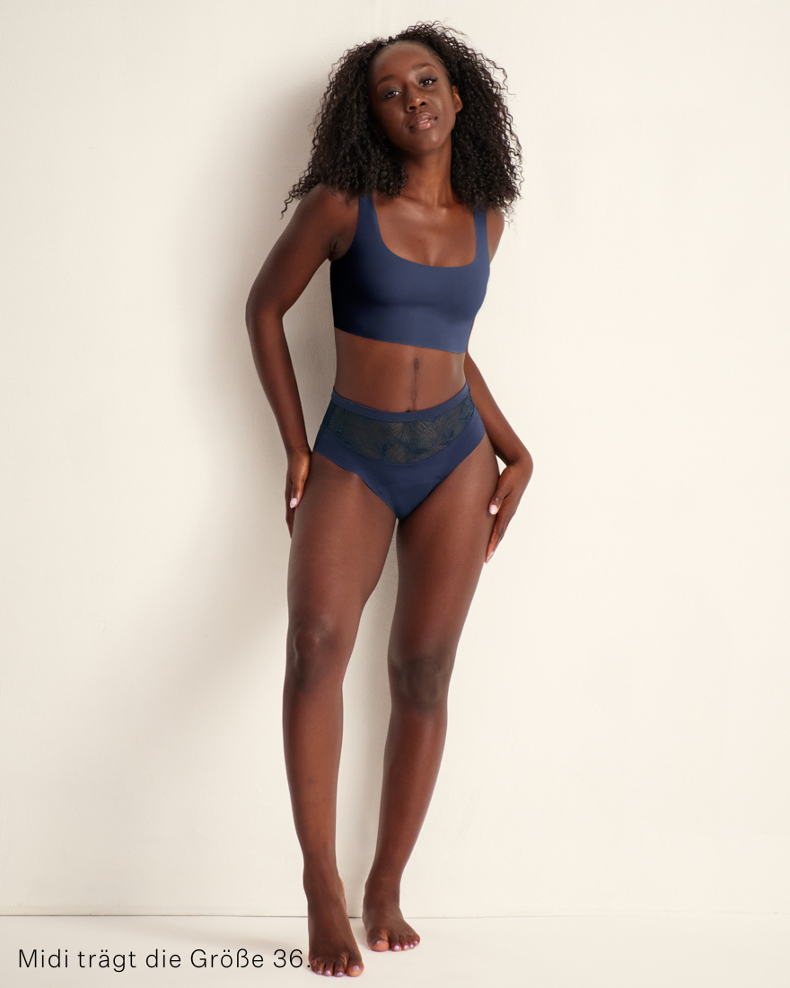 Modell trägt Periodenunterwäsche Highwaist Seamless Lace extra stark in dunkelblau mit nahtlosem Design mit breiter Spitze am Bund.
Stehend