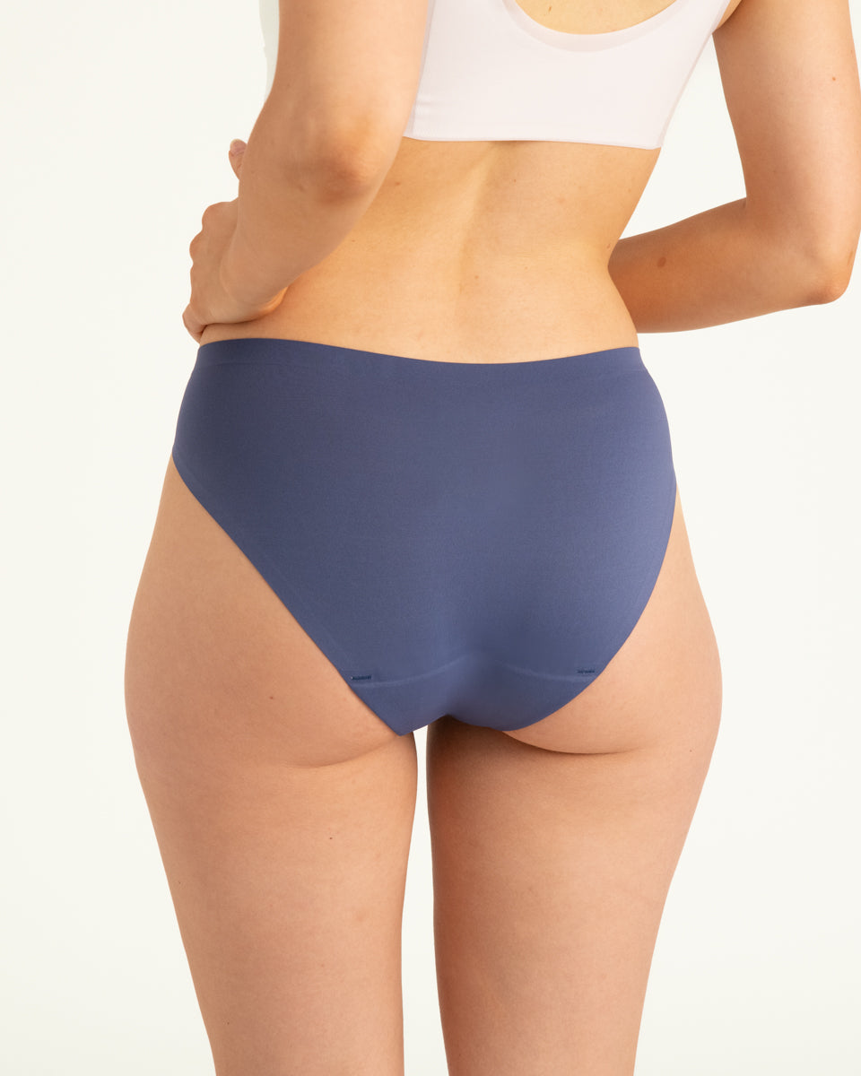 Modell trägt ooia Slip Seamless in Smoky Blue – nahtlose Periodenunterwäsche im klassischen Schnitt. Rückansicht.