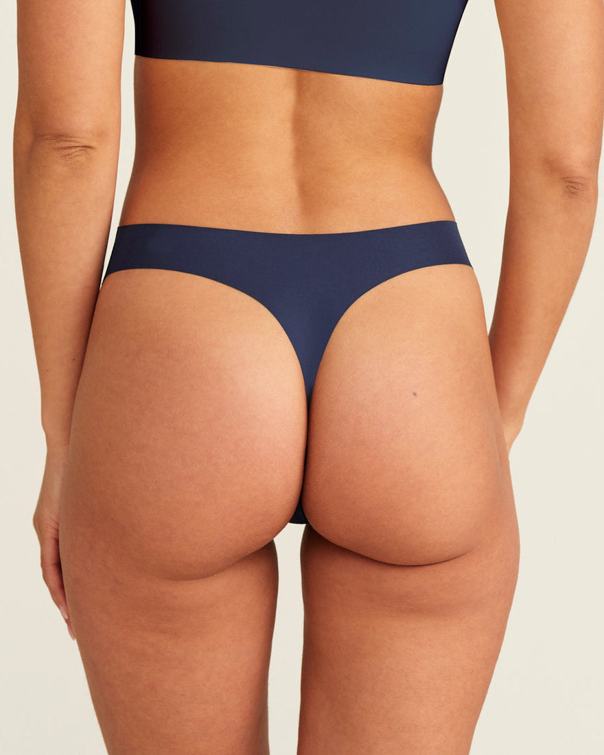Modell trägt den ooia Periodenunterwäsche String Seamless in midnight mit leichter Saugstärke, Rückansicht