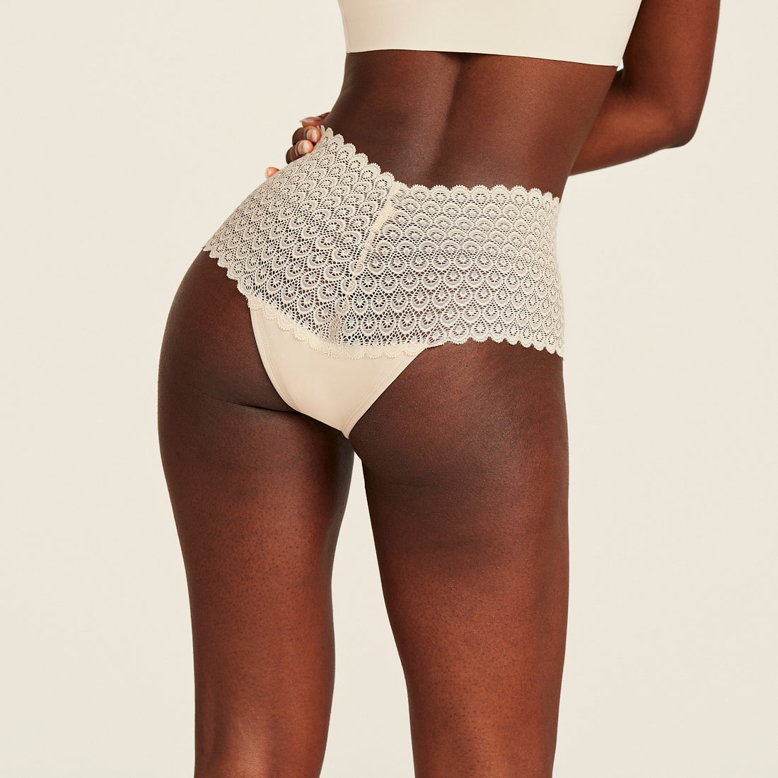 Modell trägt ooia Highwaist Comfy Lace in Ivory - Periodenunterwäsche mit hohem Bund und durchgängiger Spitze. Rückansicht.